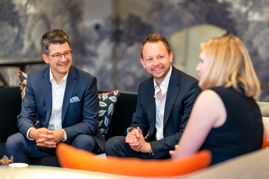 2 men and 1 woman sat talking on orange sofa 