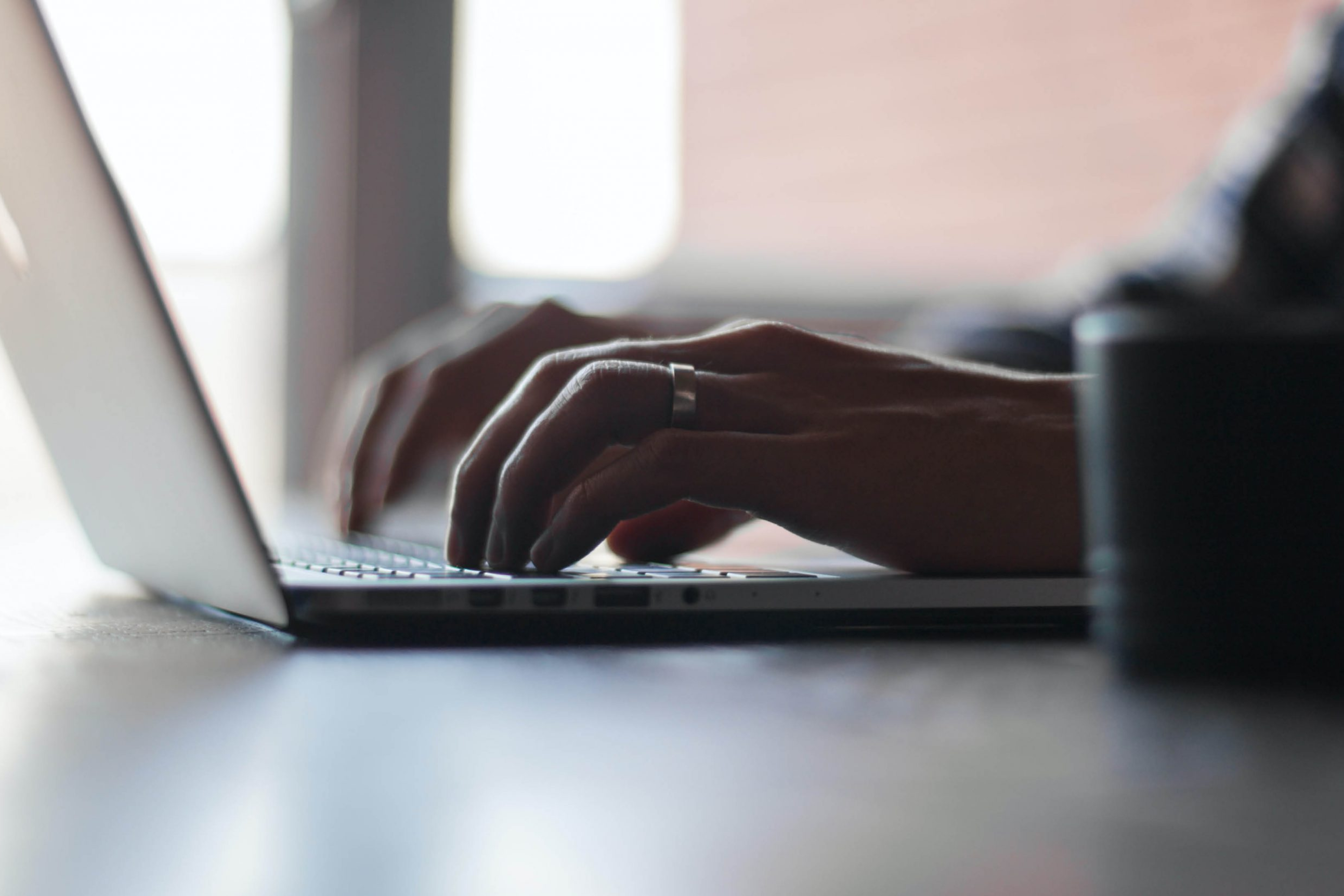 Close-up of hands typing on a laptop keyboard in soft, natural light. 