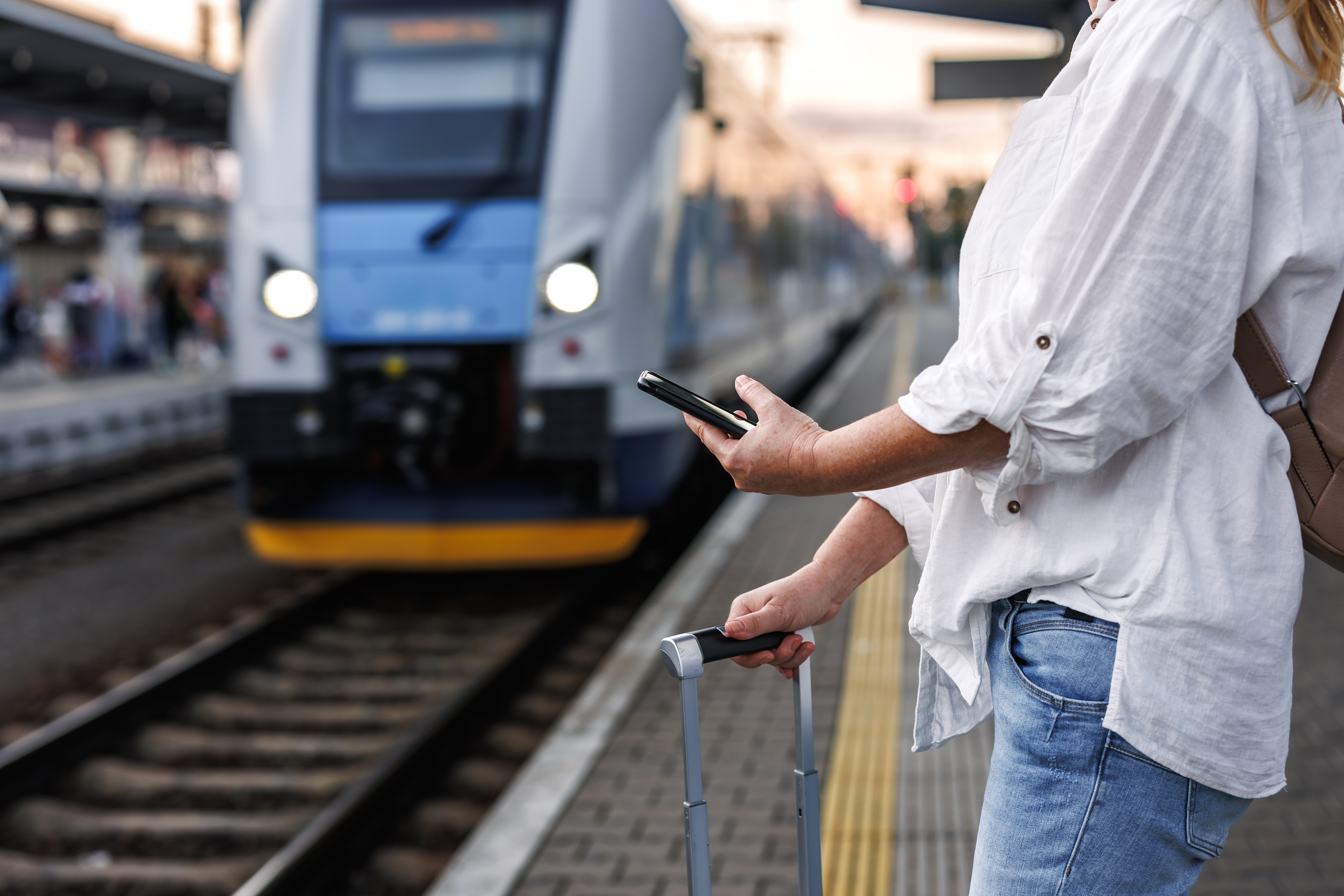 Person on their phone waiting for a train holding a suitcase
