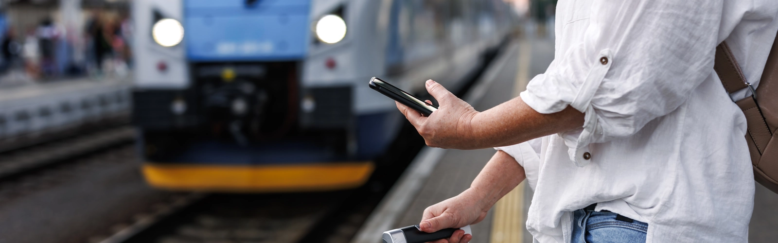 Person on their phone waiting for a train holding a suitcase Person on their phone waiting for a train holding a suitcase