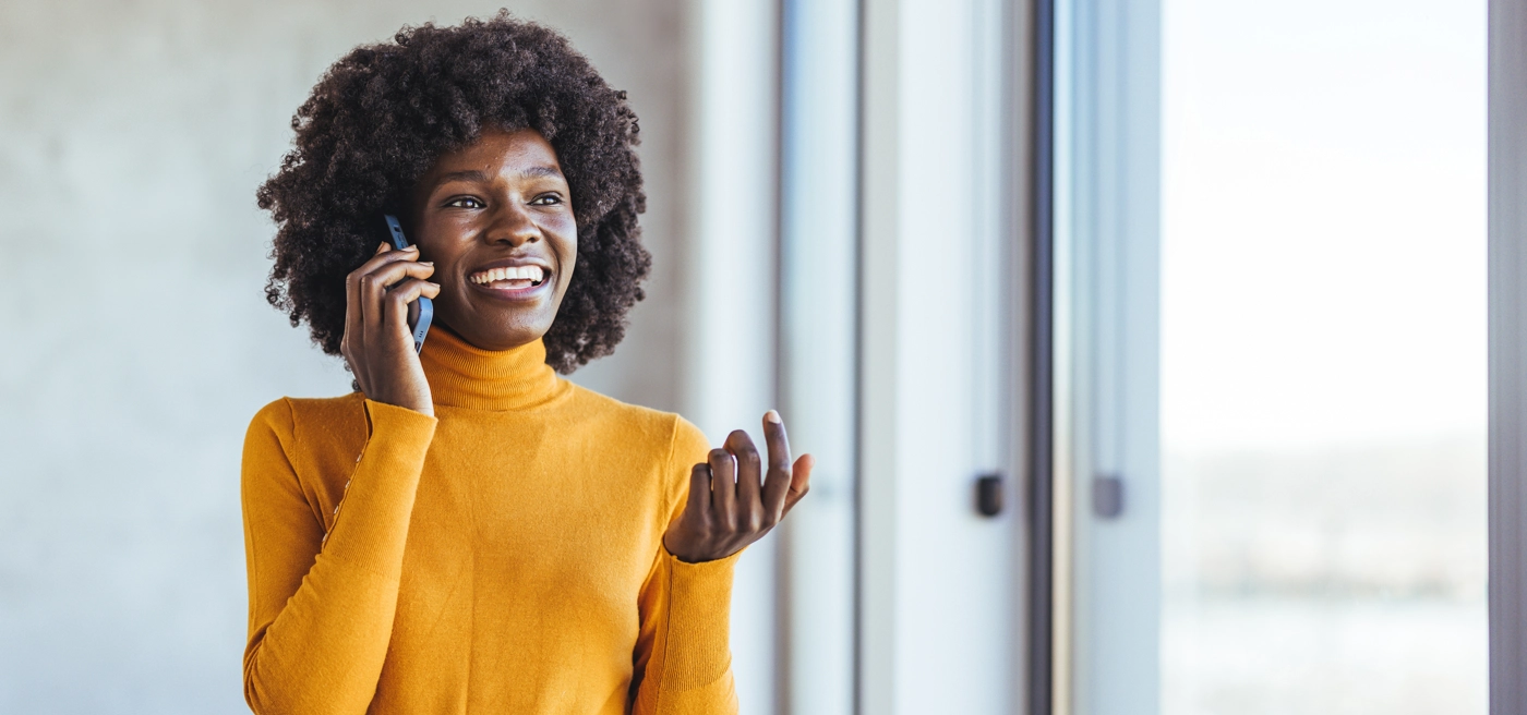 Smiling woman talking on phone near window, wearing yellow sweater Smiling woman talking on phone near window, wearing yellow sweater