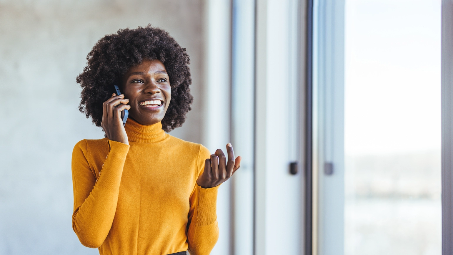 Smiling woman talking on phone near window, wearing yellow sweater Smiling woman talking on phone near window, wearing yellow sweater