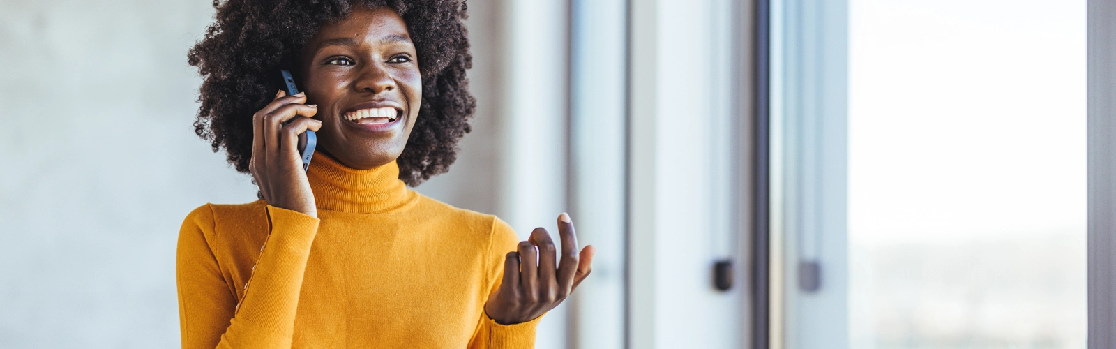 Smiling woman talking on phone near window, wearing yellow sweater Smiling woman talking on phone near window, wearing yellow sweater