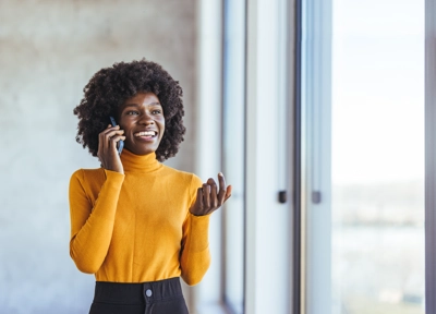Smiling woman talking on phone near window, wearing yellow sweater Smiling woman talking on phone near window, wearing yellow sweater