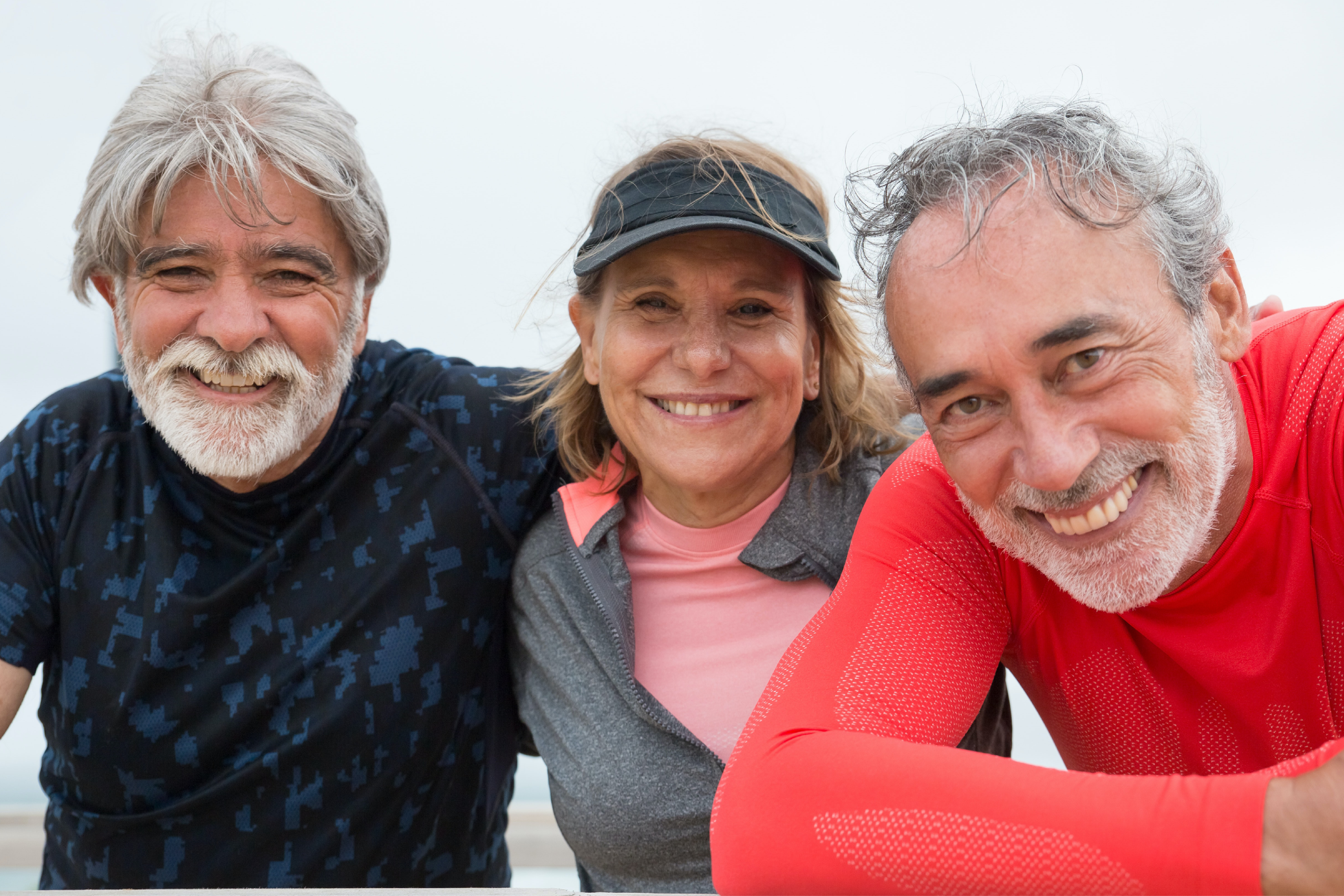 Three smiling older adults in athletic clothing posing closely together outdoors.