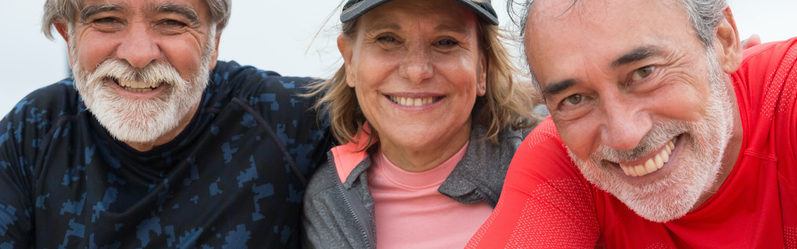 Three smiling older adults in athletic clothing posing closely together outdoors. Three smiling older adults in athletic clothing posing closely together outdoors.
