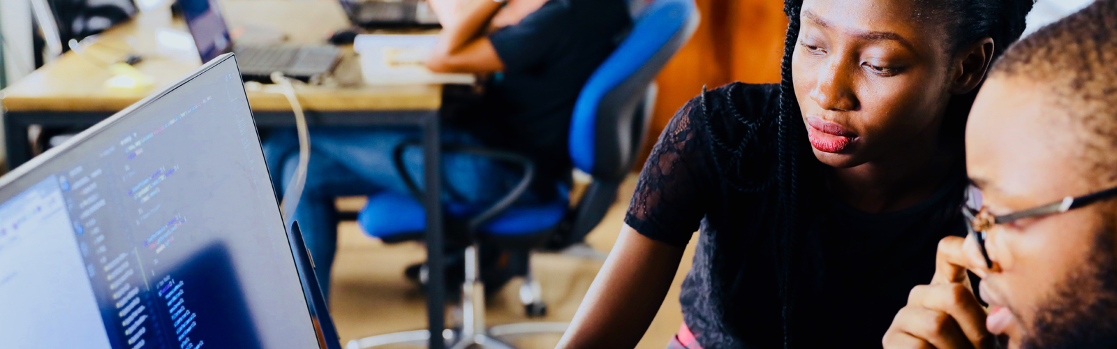 A woman points at code on a laptop screen while working with a colleague in a shared office space A woman points at code on a laptop screen while working with a colleague in a shared office space