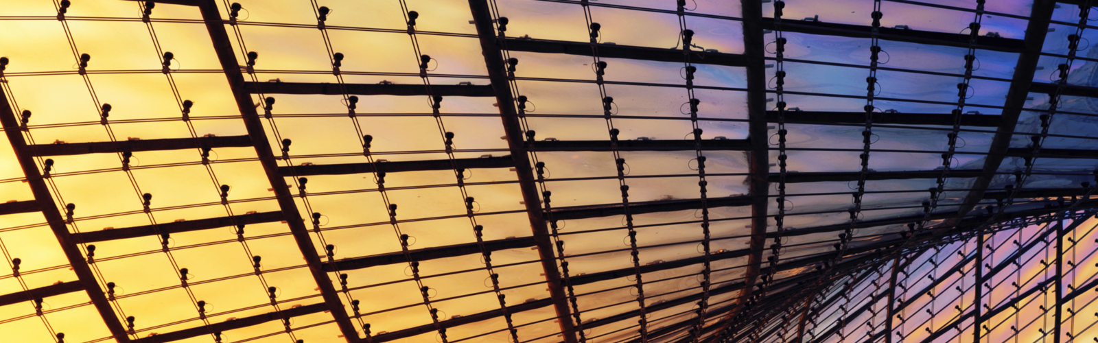Curved glass and steel ceiling structure glowing with warm yellow and cool purple light. Curved glass and steel ceiling structure glowing with warm yellow and cool purple light.