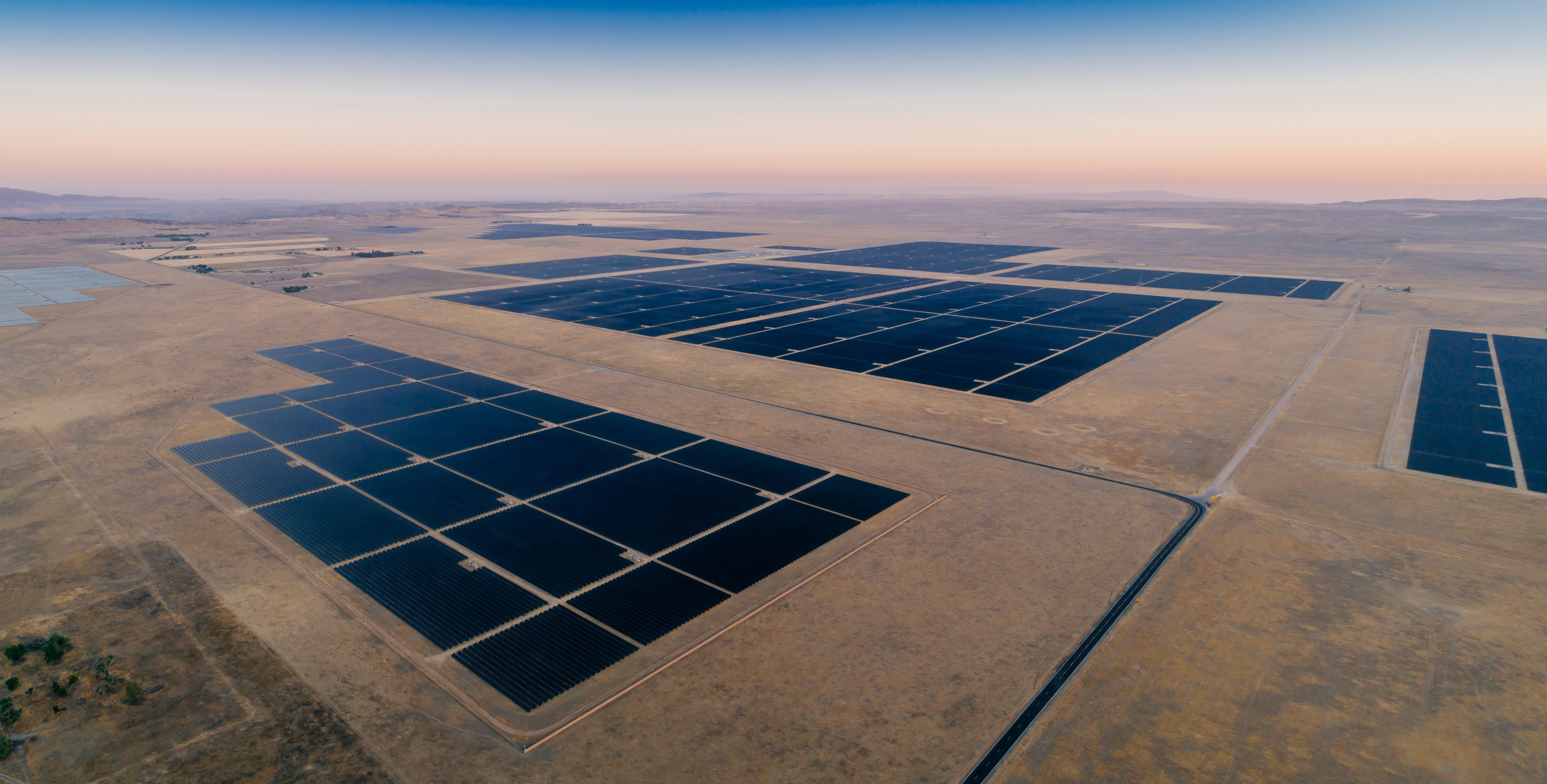 Massive solar farm stretching across desert landscape beneath soft pastel sunrise skies.