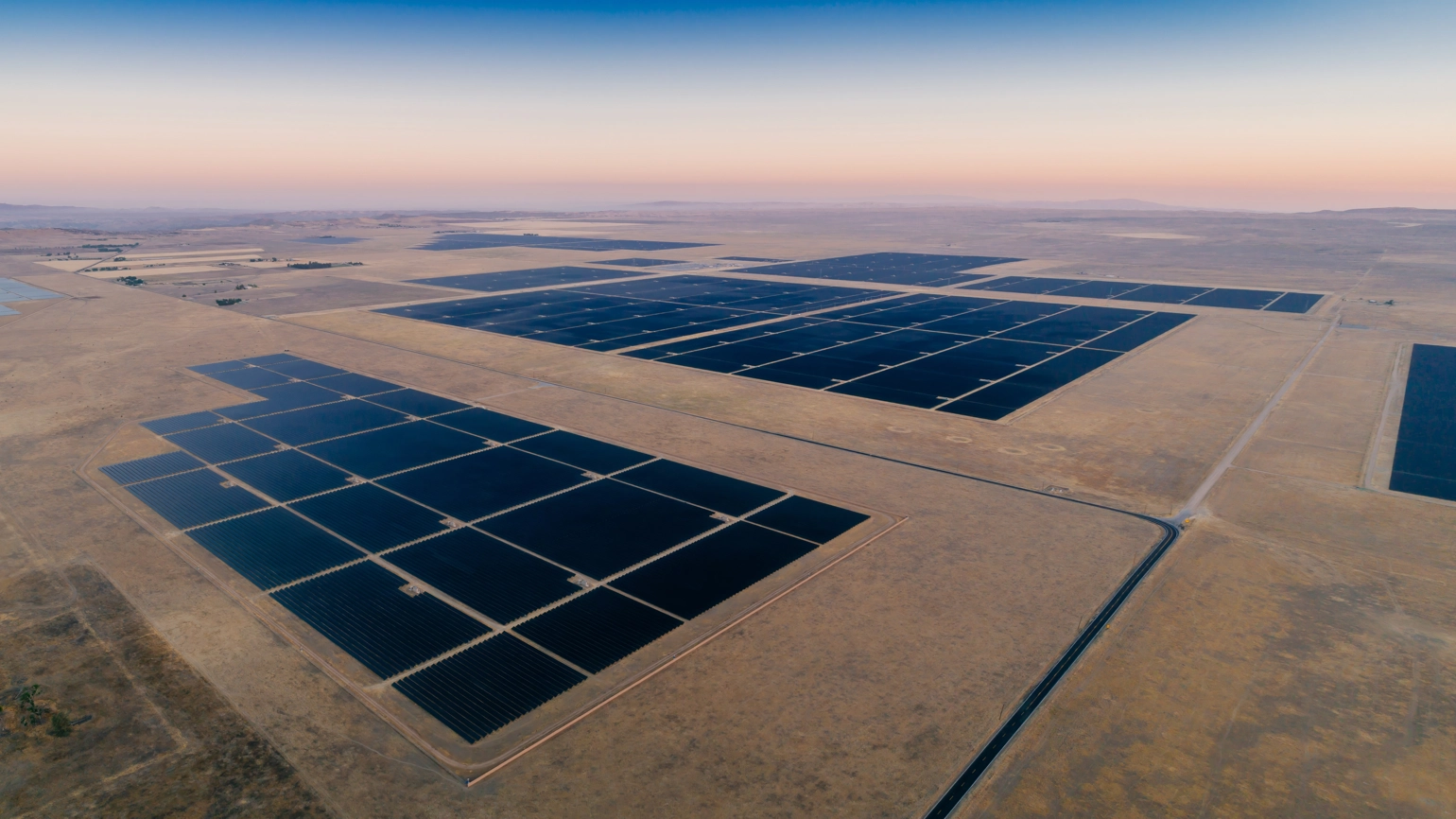 Massive solar farm stretching across desert landscape beneath soft pastel sunrise skies. Massive solar farm stretching across desert landscape beneath soft pastel sunrise skies.