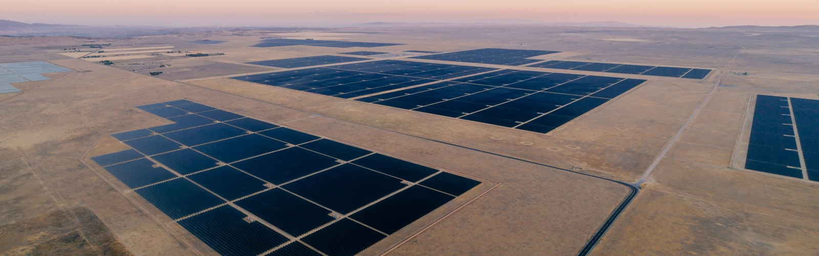 Massive solar farm stretching across desert landscape beneath soft pastel sunrise skies. Massive solar farm stretching across desert landscape beneath soft pastel sunrise skies.